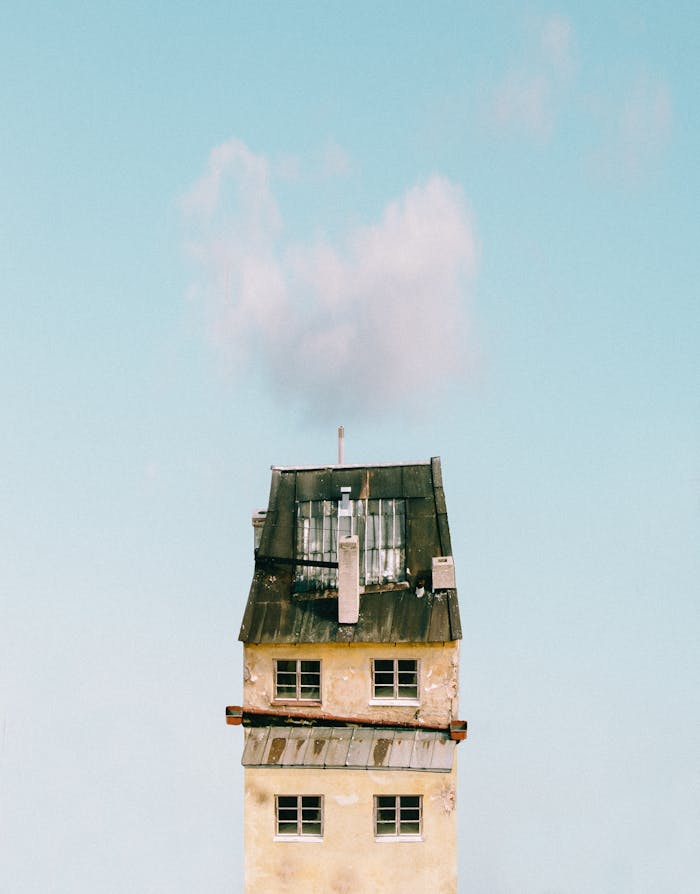 A minimalist photograph of a tall, simple urban tower against a clear blue sky with clouds.